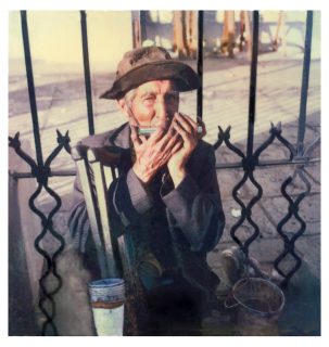 An old man plays a harmonica against a wrought iron gate, Central Park, Guatemala City